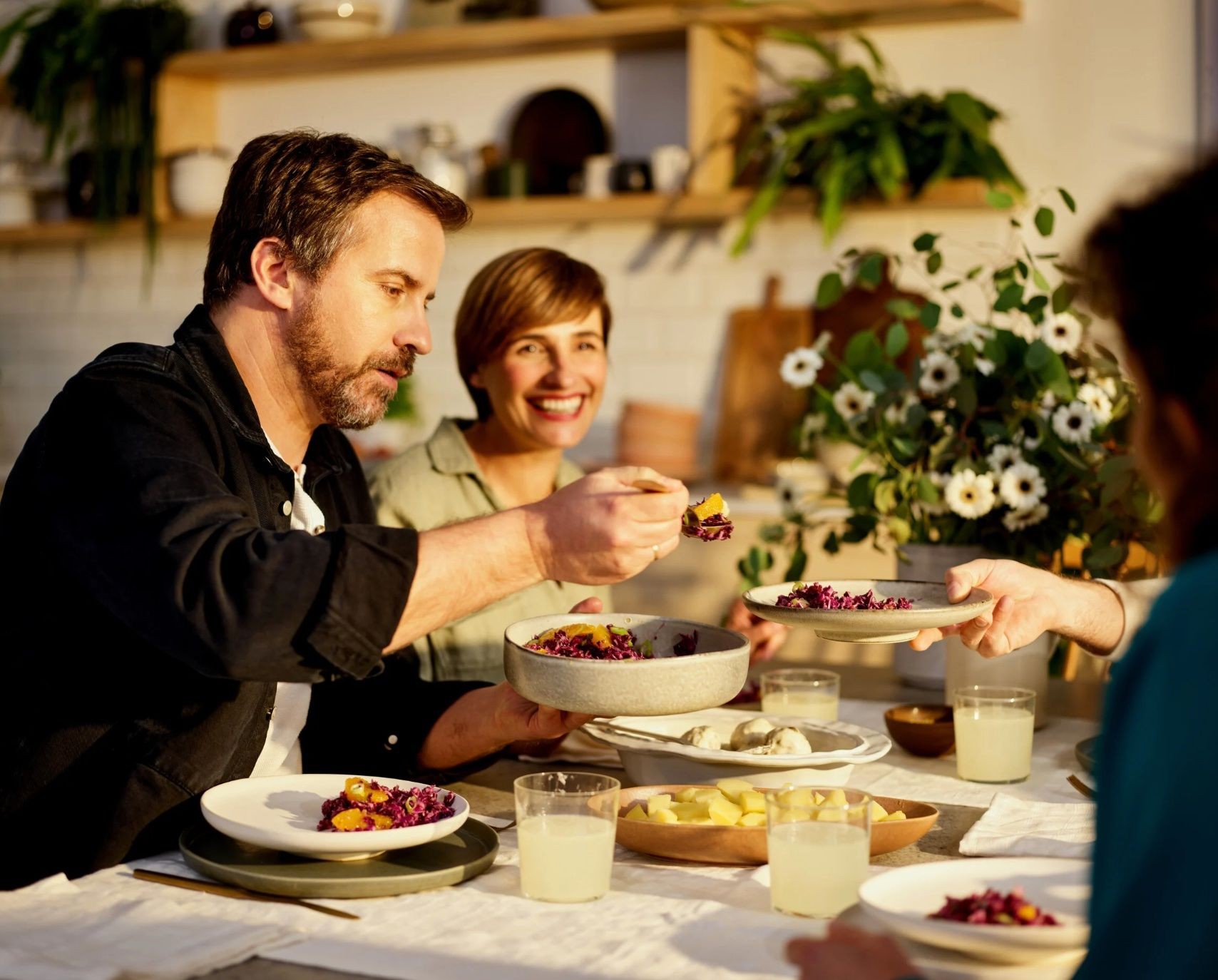 Group of people enjoying a meal together at a dining table with decorative plants and dishes.